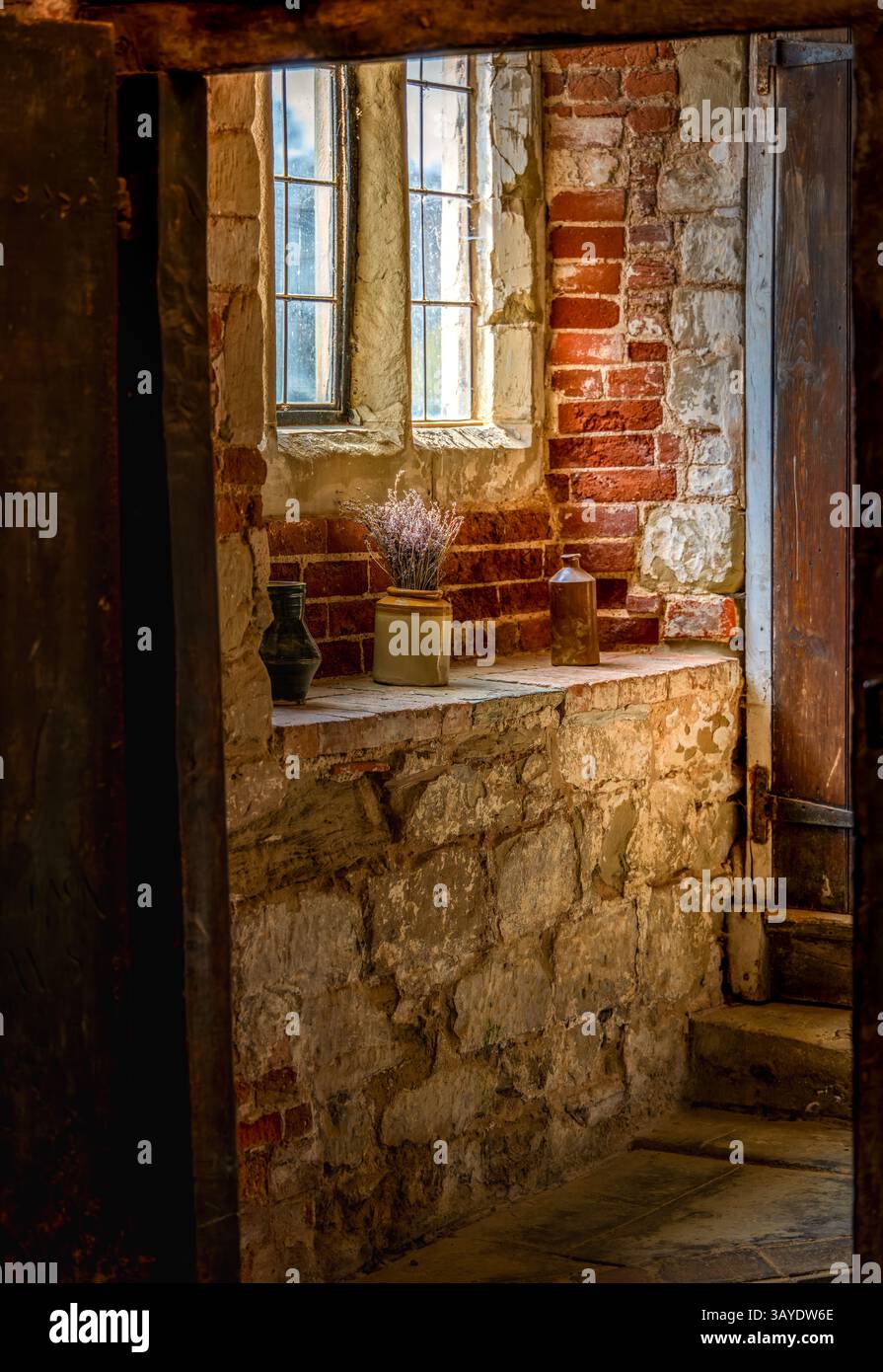 Sanftes Licht offenbart eine zeitlose Steinfensterbank mit getrocknetem Lavendel in einer rustikalen Ecke aus mittelalterlichem Backstein und altem Holz Stockfoto