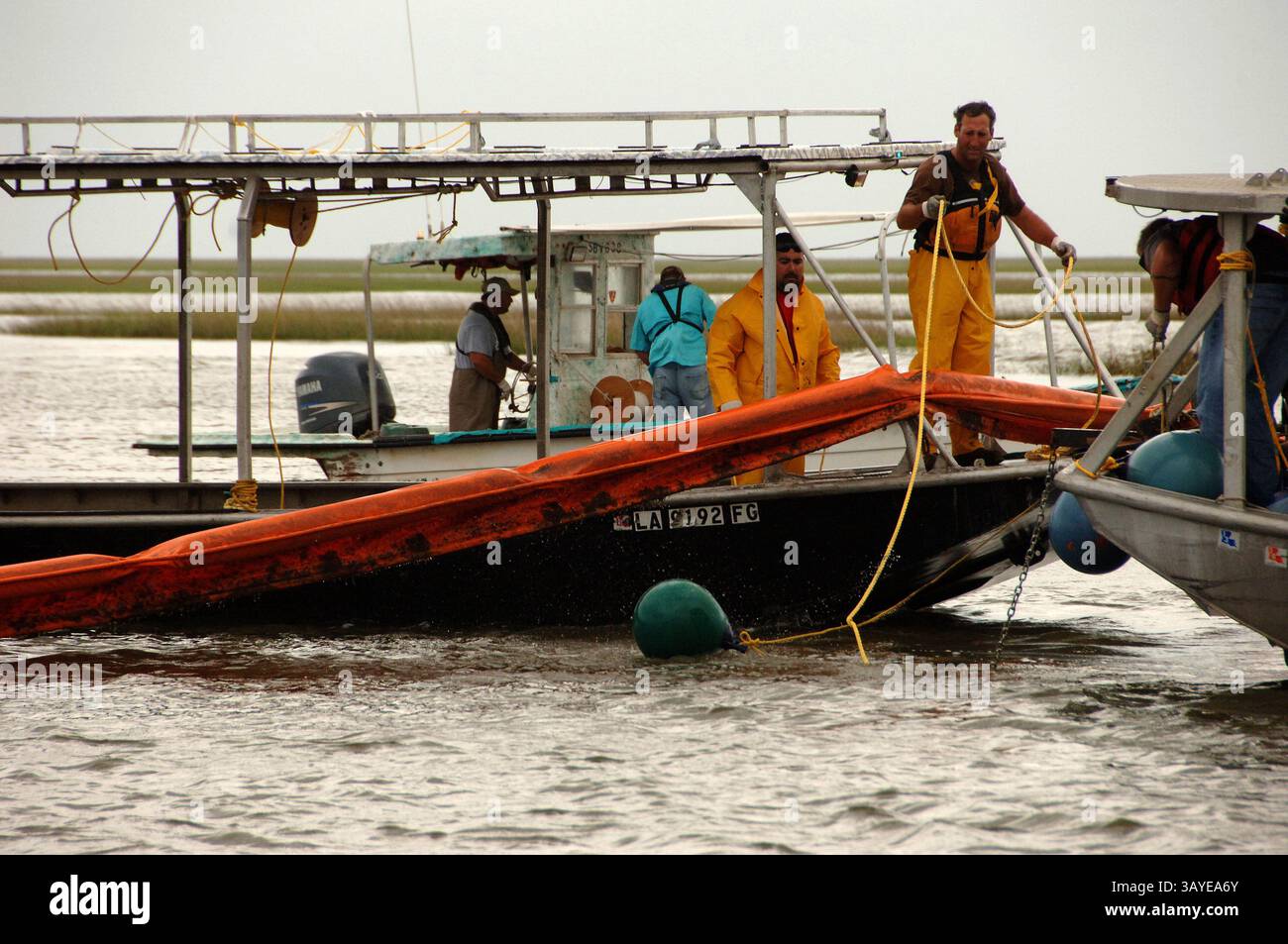 29. Juni 2010 – Lake Barre, Louisiana, USA – Bauunternehmer arbeiten schnell daran, einen Anker für Hard Boom zu installieren, der sich über einen Pass zwischen Sumpfgras in Lake Barre, La, erstreckte, während die äußeren Bänder des Tropical Storm Alex am Dienstag den Himmel verdunkeln. Da das schlechte Wetter durch den Sturm die Bedingungen für den Wasserbetrieb in den nächsten Tagen unsicher machen könnte, schlossen Bauunternehmer und Mitarbeiter der Küstenwache in Branch Terrebonne Parish, La. Pässe mit diesen schwimmenden Barrieren ab, um zu verhindern, dass Öl aus dem Deepwater Horizon in den See gelangt Stockfoto