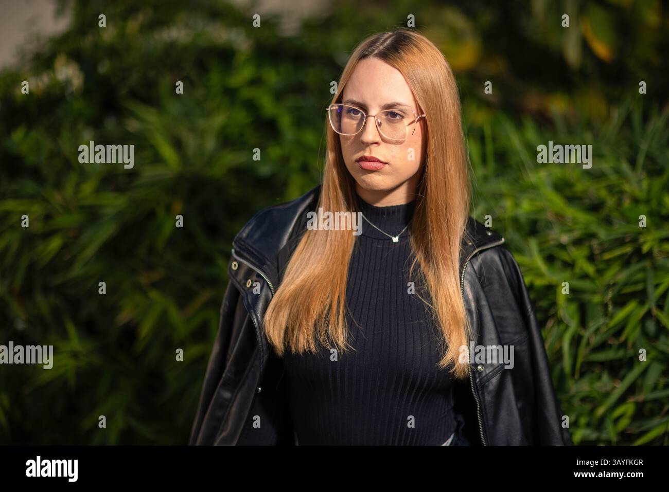 Stilvolle Frau aus Leder und Denim mit einem ernsten Ausdruck unter hellem Sonnenlicht Stockfoto