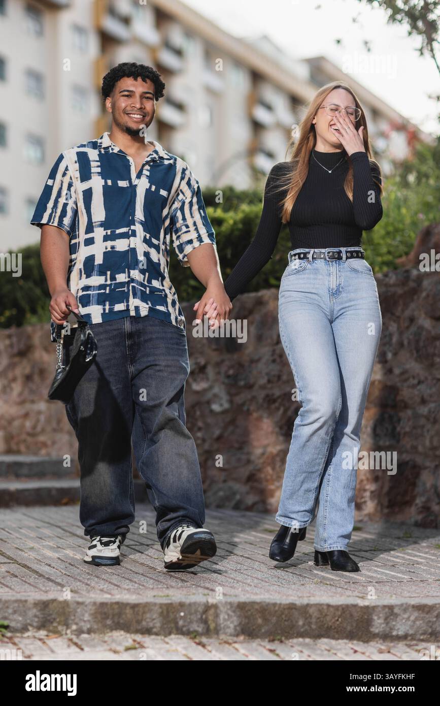Glückliches junges Paar, das Hand in Hand im Freien in urbaner Umgebung geht Stockfoto