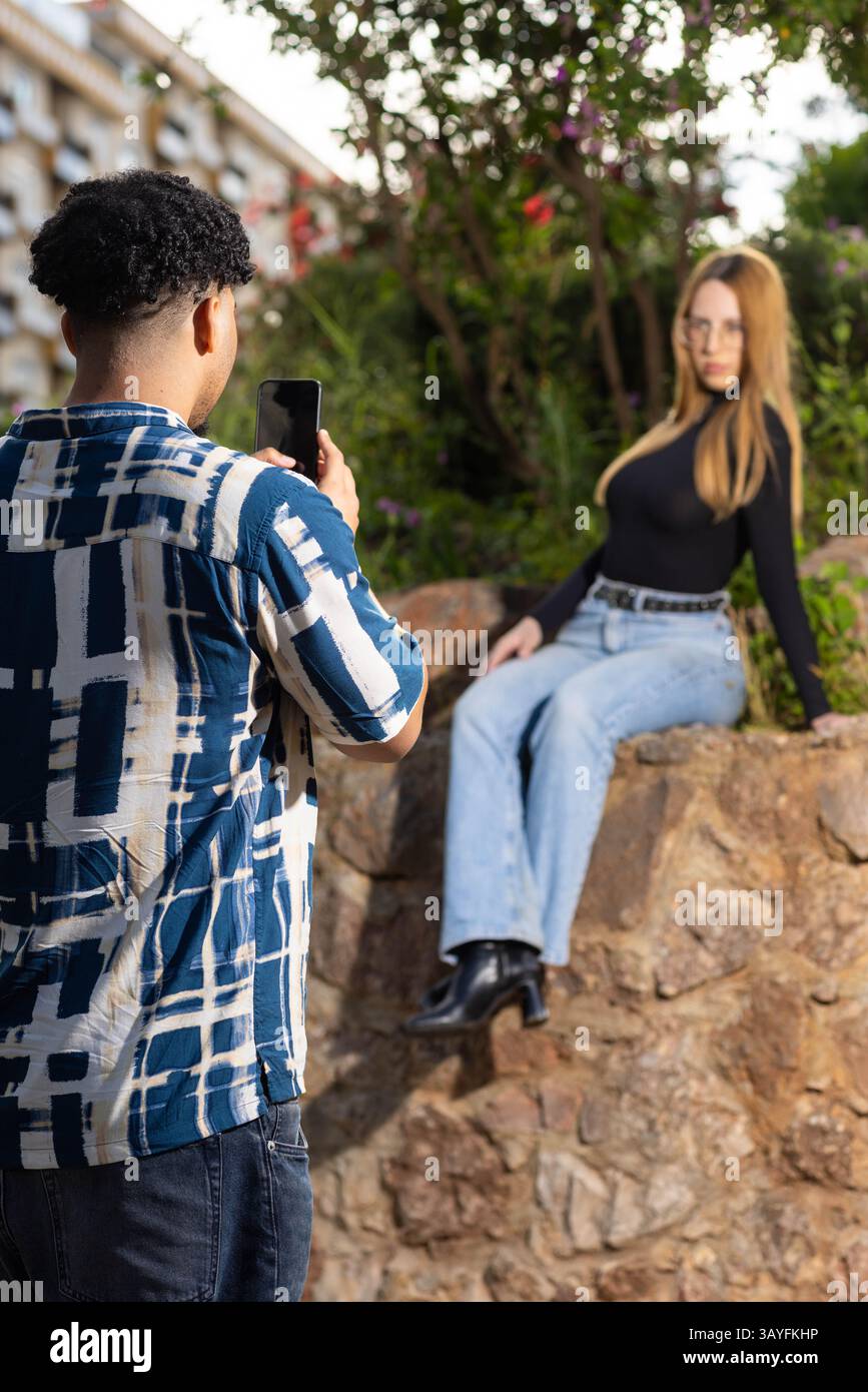Junge Frau posiert auf einer Steinmauer, während sie draußen in einem zwanglosen Urban Garden Fotoshooting die Kamera anlächelt Stockfoto