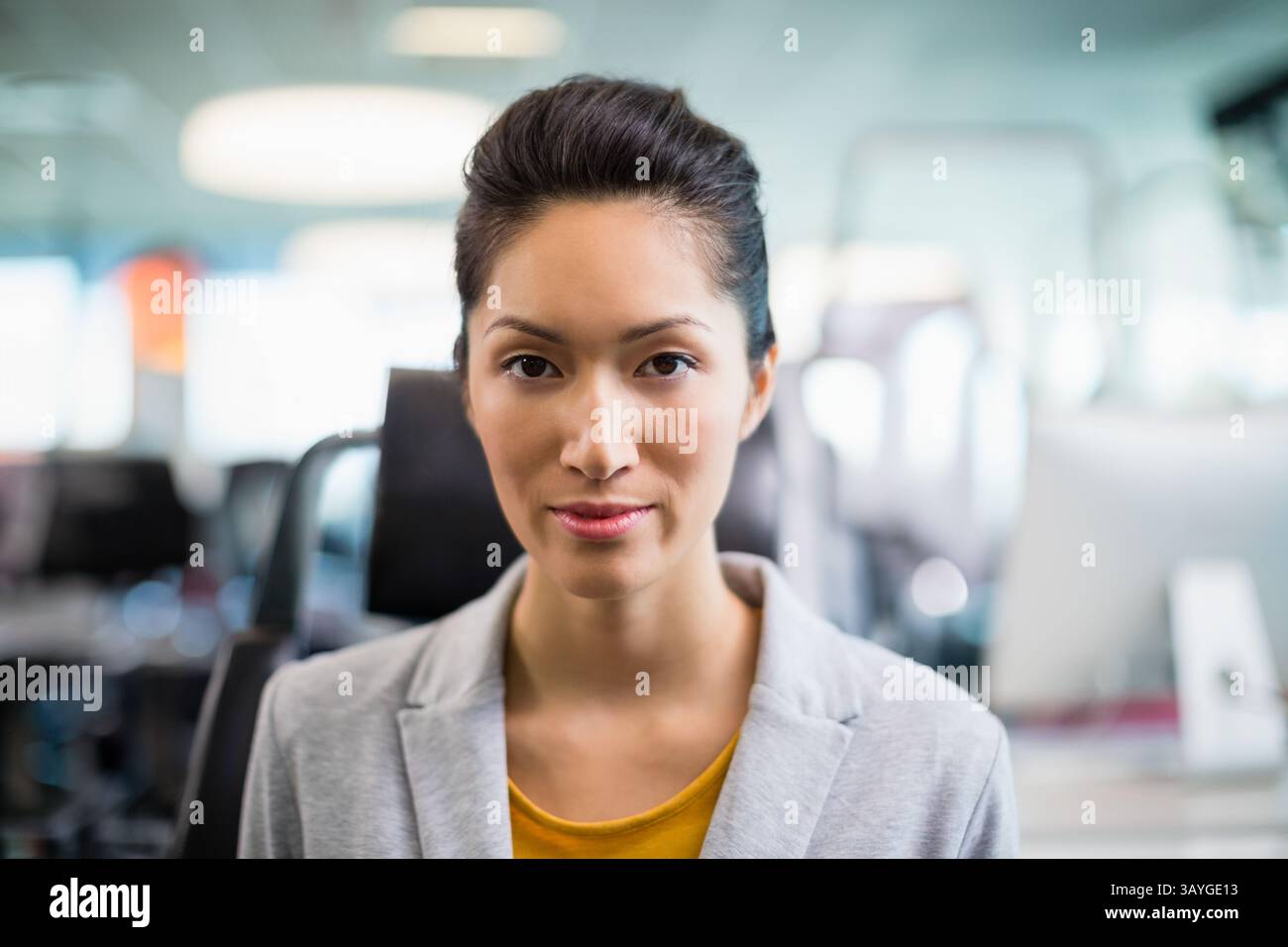 Junge Erwachsene chinesische Geschäftsfrau, die im Büro zwischen Monitoren und Deckenleuchten sitzt Stockfoto