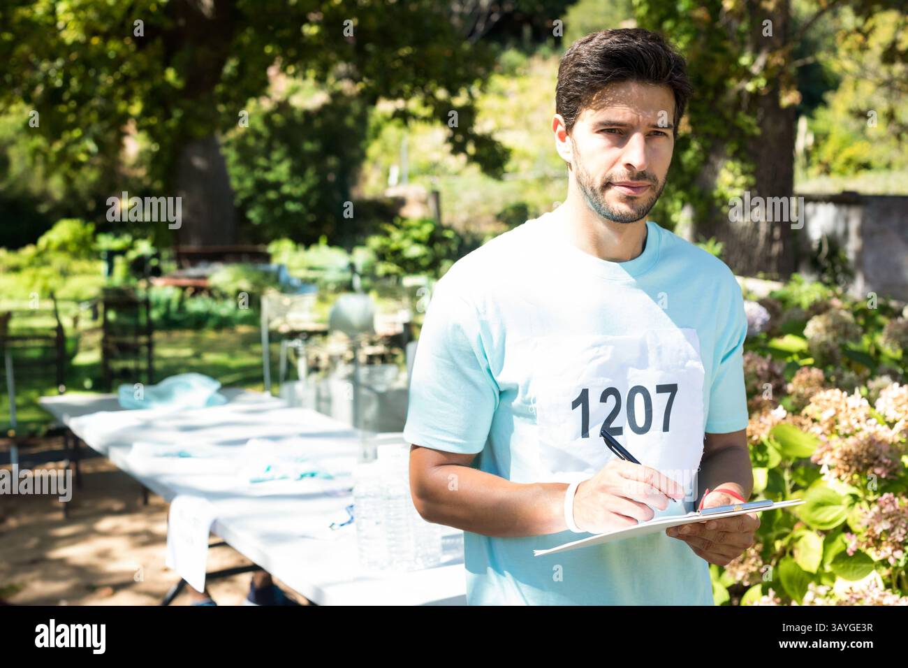 Mittelgroßer Mann mit Race Lätzchen 1207, stehend am Klapptisch in grünem Park, der auf dem Klemmbrett steht Stockfoto