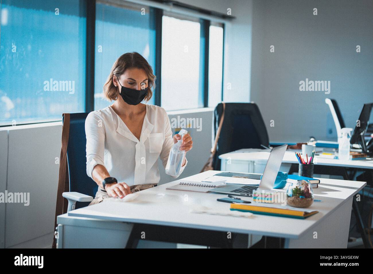 Büroangestellter Reinigungstisch im offenen Büro, mit Sprühflasche und Tuch in der Nähe des Laptop-Terrariums Stockfoto
