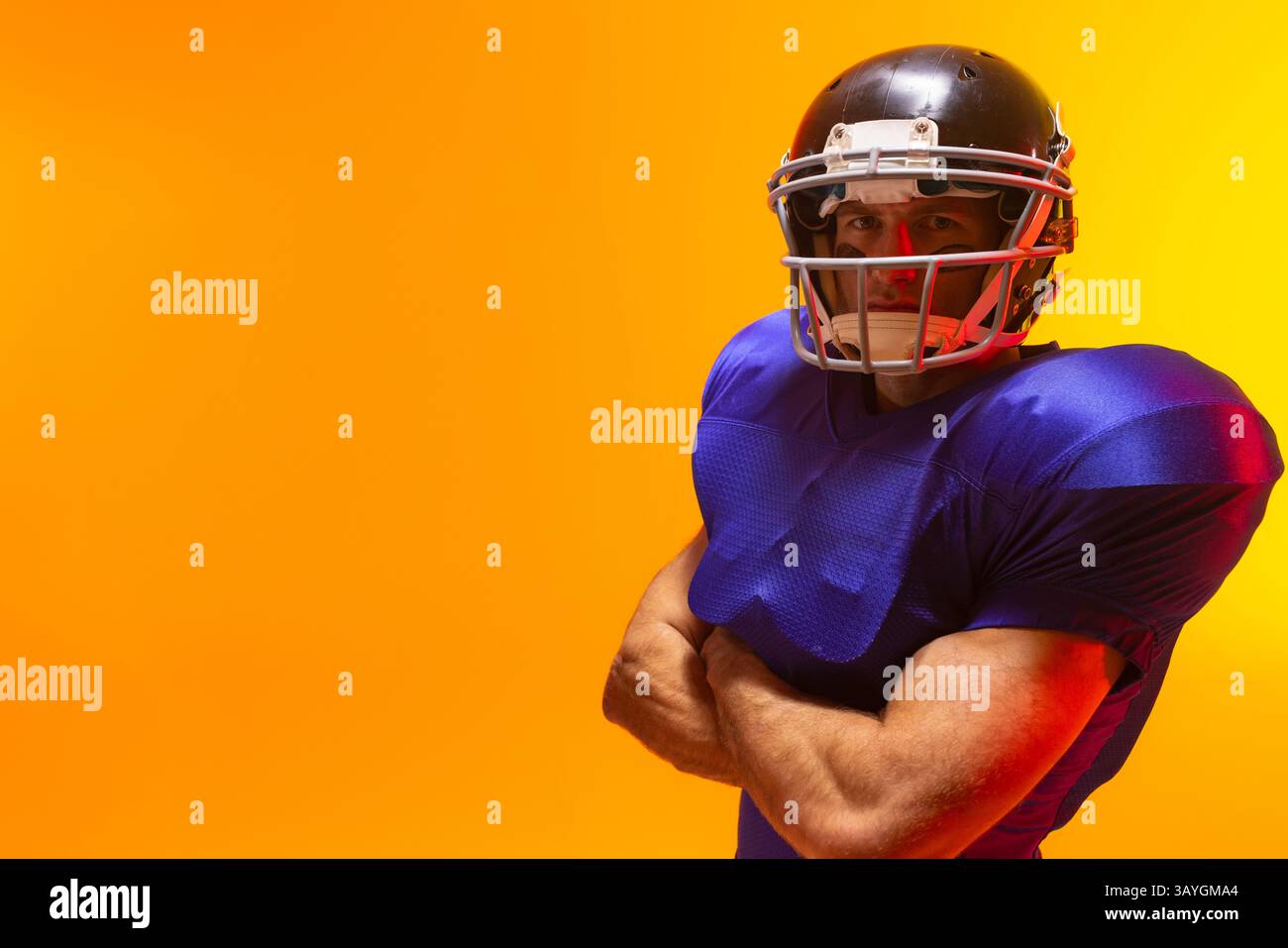 Mann mit mittlerem Erwachsener, amerikanischer Fußballspieler, der im orangen Studio steht, mit Helm und Polstern, Kopierraum Stockfoto