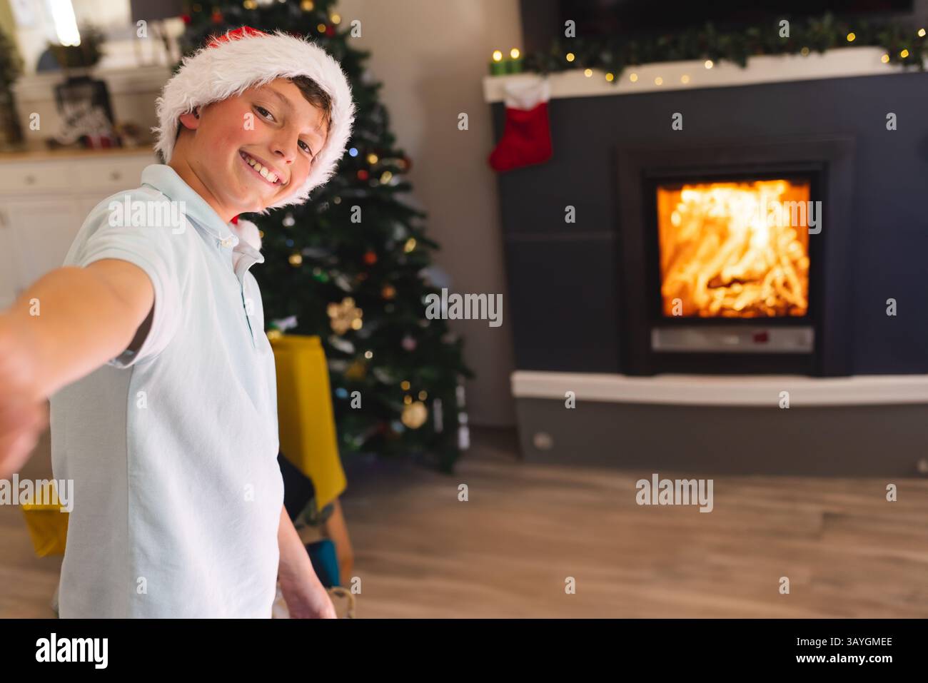 Junge, der zu Hause steht mit Weihnachtsbaum, Weihnachtsmann-Hut, Strumpf, Girlanden Lichtern, Kopierraum Stockfoto