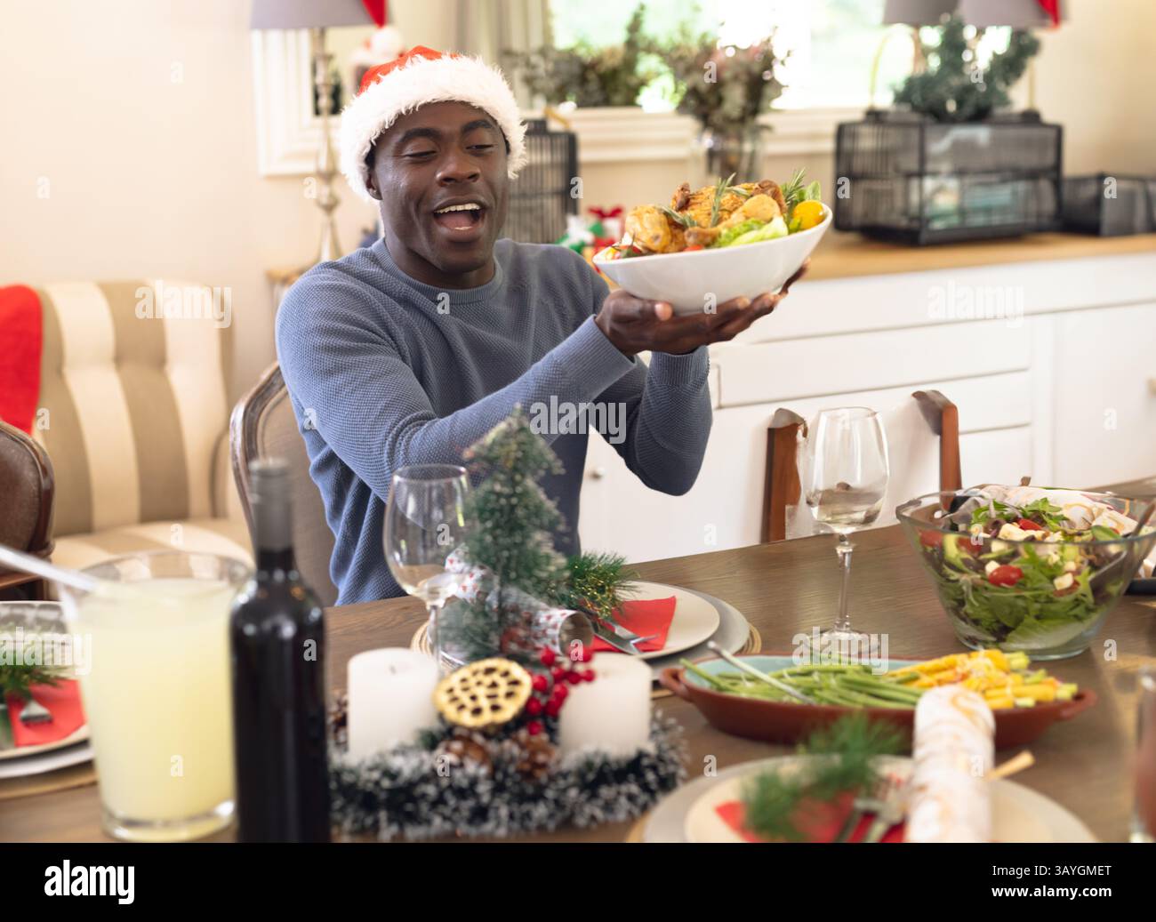 Afroamerikaner mit Weihnachtsmann-Hut, lächelnd und mit einer Hühnerschale am Esstisch zu Hause Stockfoto