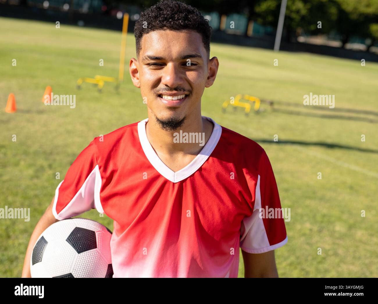 Männlicher Fußballspieler, der auf dem Outdoor-Trainingsfeld Übungen macht und den Ball mit Kegeln und Hürden hält Stockfoto