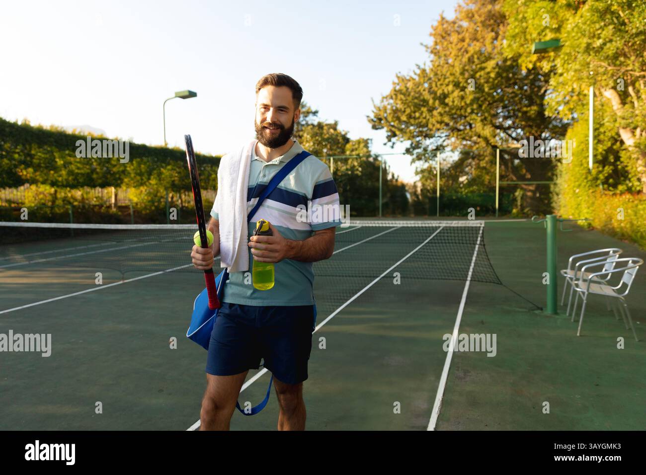 Mann, der auf einem Tennisplatz im Freien läuft, Schläger trägt, eine grüne Wasserflasche und eine Sporttasche hält Stockfoto