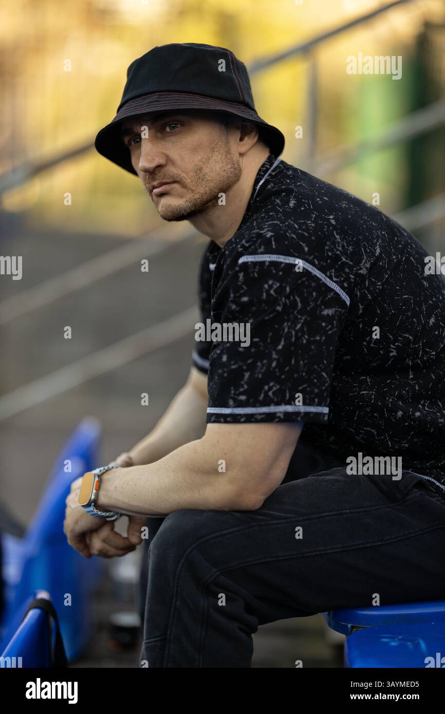 Individuelle Bechermütze und legere Kleidung sitzen auf blauen Tribünen, die sich auf die Veranstaltung konzentrieren, die sich vor ihnen bei weichem Tageslicht abspielt Stockfoto