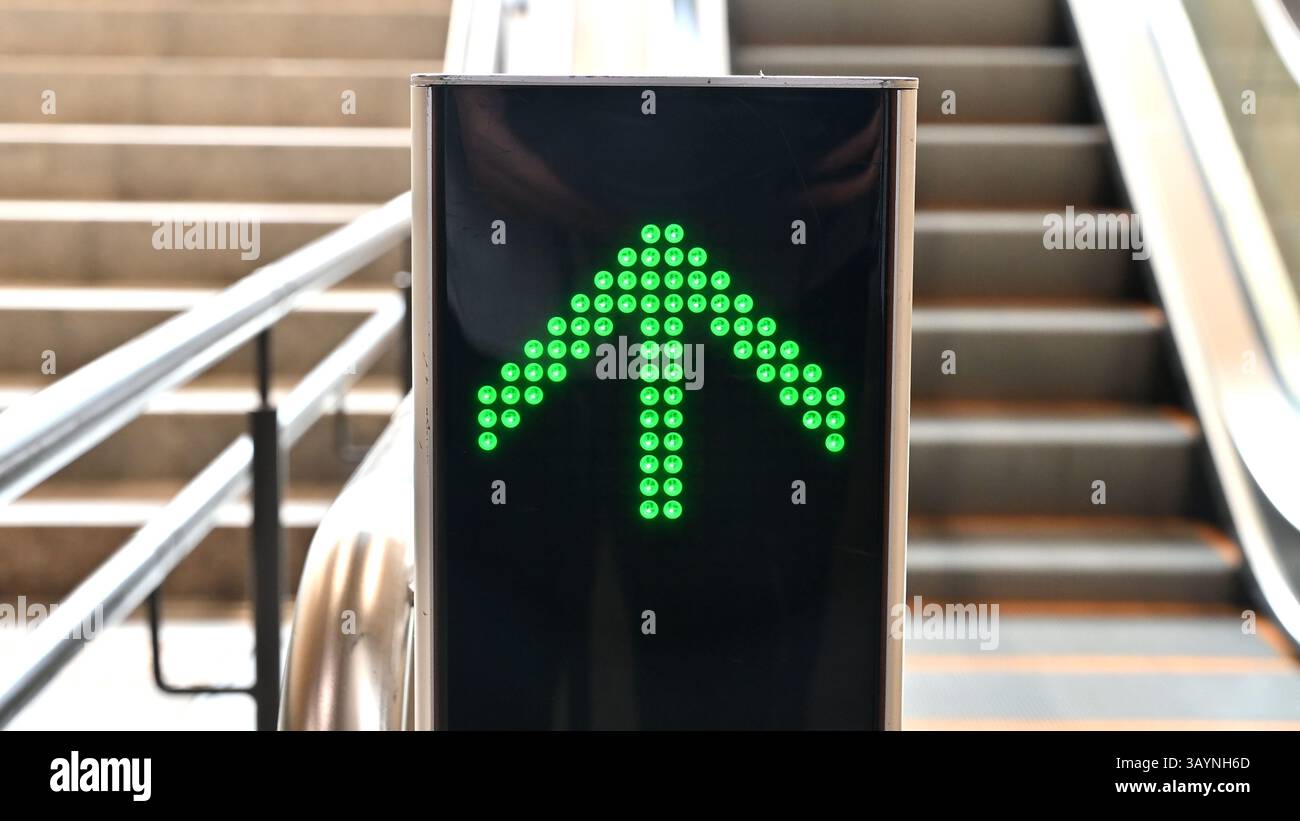 Nahaufnahme eines leuchtenden grünen Pfeil-LED-Schilds, das die Aufwärtsrichtung einer Rolltreppe anzeigt. Stockfoto