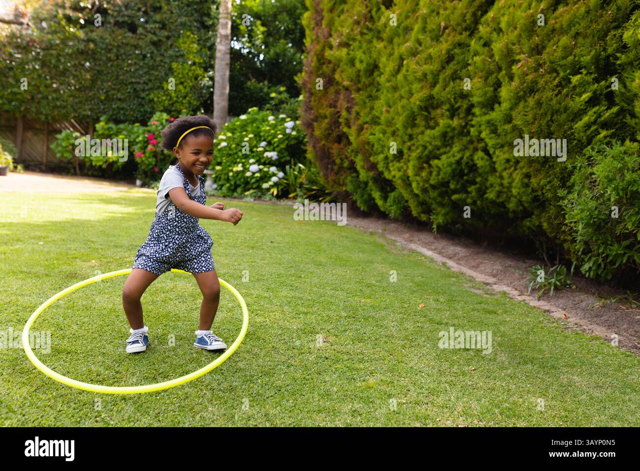 6-jähriges afroamerikanisches Mädchen, das mit hellgelbem Hula Hoop auf dem Rasen im Garten spielt Stockfoto