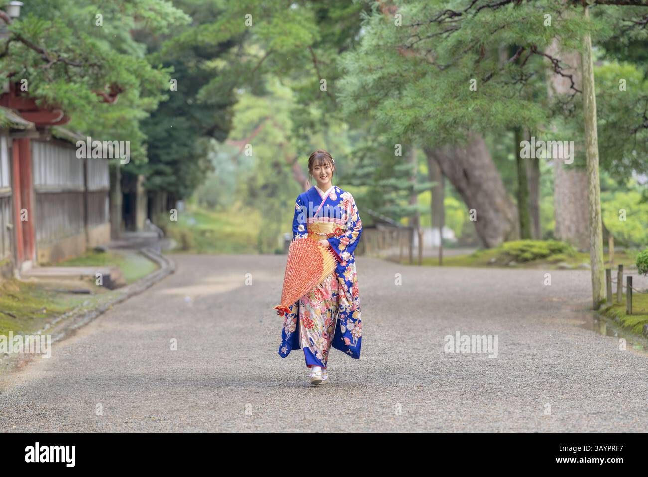 Eine lokale Stadt in Japan an einem verregneten Sommertag. Japanische Frau, die einen blauen Kimono für Teenager trägt, mit einem japanischen Regenschirm, der durch ein traditionelles Kleid läuft Stockfoto