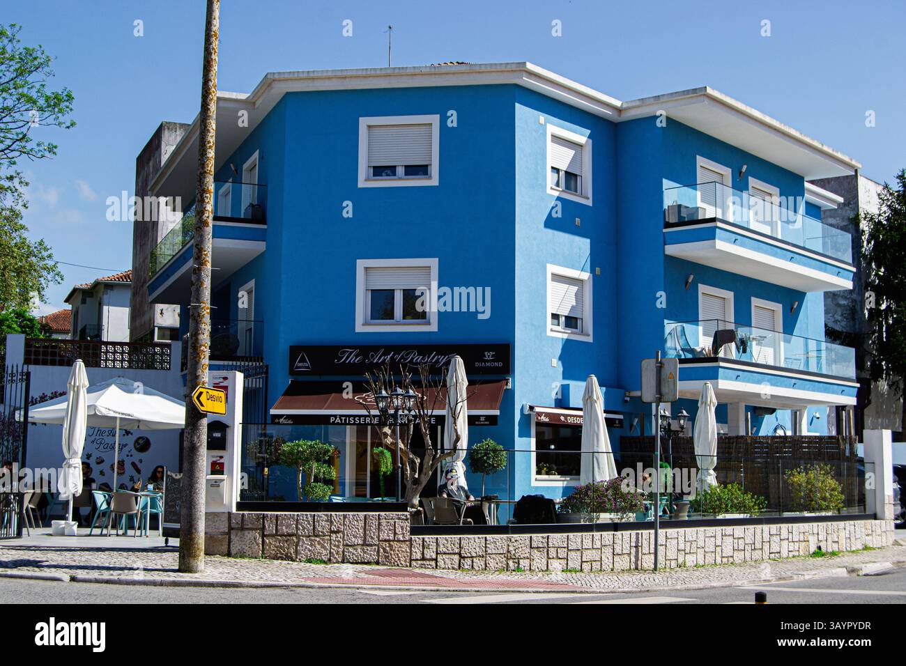 Caldas da Rainha, Portugal - 17. April 2025: Ein lebhaftes blaues Gebäude mit einem Café, umgeben von Pflanzen und Blick auf die Straße Stockfoto