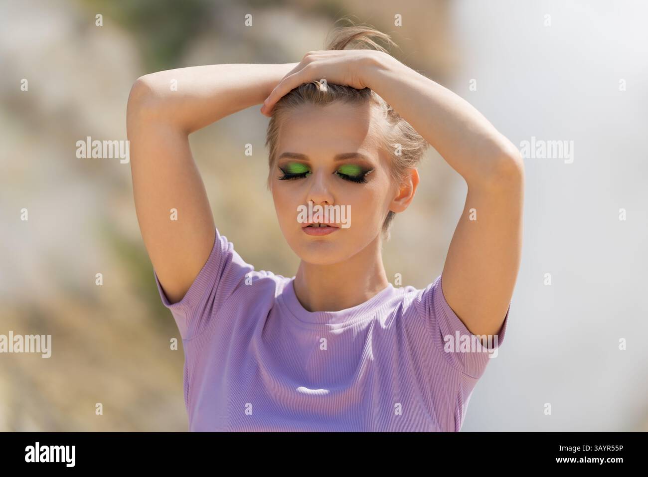 Das Sommerporträt des Models ist geschminkt und die Augen sind geschlossen. Sie hat ihre Hände in den Haaren hochgehoben. Frau posiert vor natürlicher Kulisse in vo Stockfoto