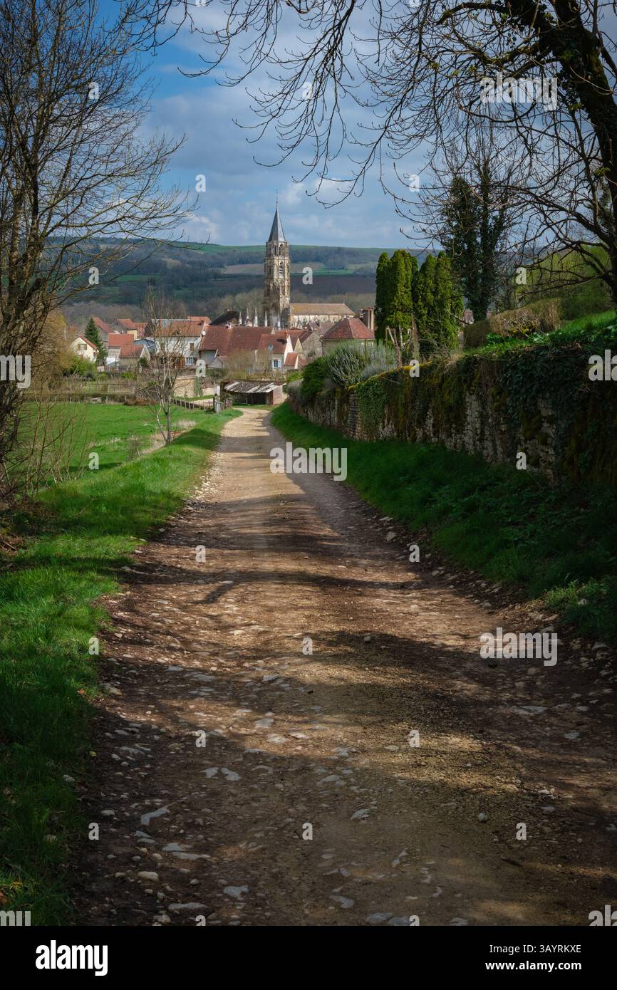 Vertikaler Blick auf einen Wanderweg, der hinunter zu einem mittelalterlichen Dorf mit Kirchturm und Vegetation führt Stockfoto