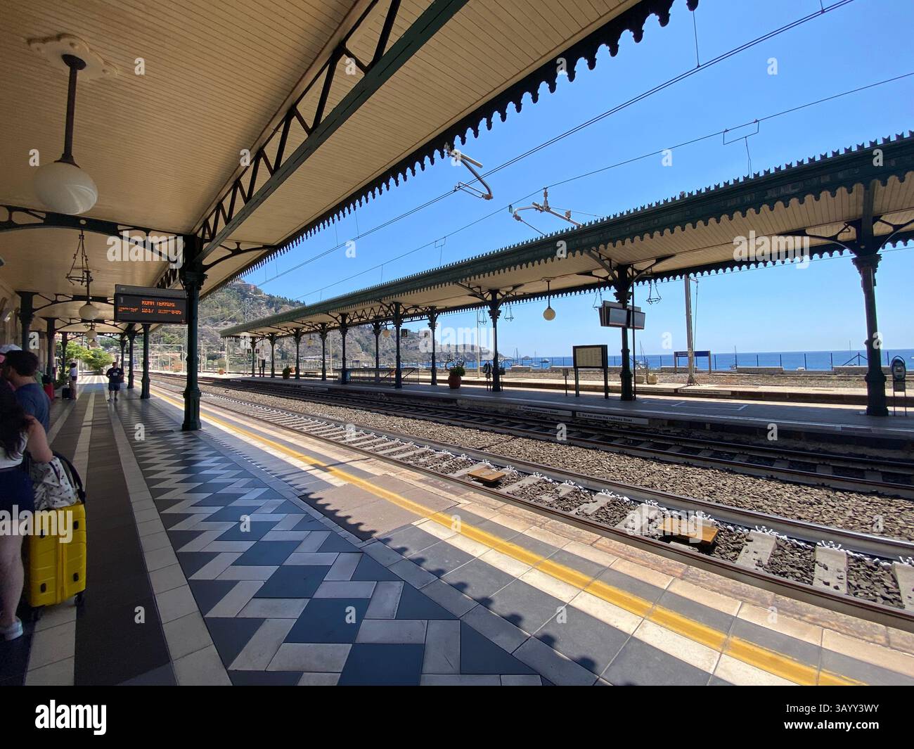 Touristen warten am Bahnhof Taormina-Giardini Naxos, mit Blick auf das Mittelmeer in malerischer sizilianischer Küstenlandschaft Stockfoto