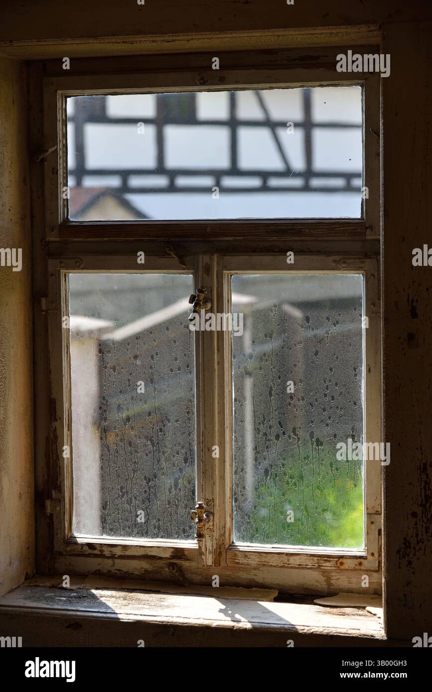 Ein Blick auf ein traditionelles Fachwerkhaus durch eine schmutzige Fensterscheibe. Stockfoto