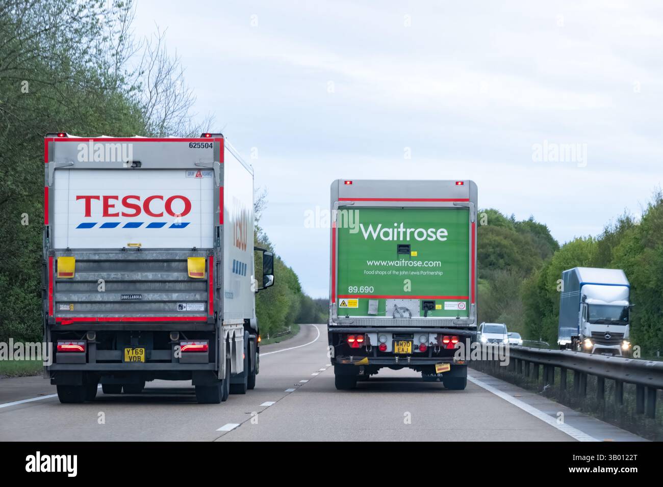 UK. Ein Waitrose-Lastwagen überholt einen Tesco-Lastwagen auf der Autobahn. Das Heck der Lastwagen zeigt deutlich die Marke der Supermärkte Stockfoto