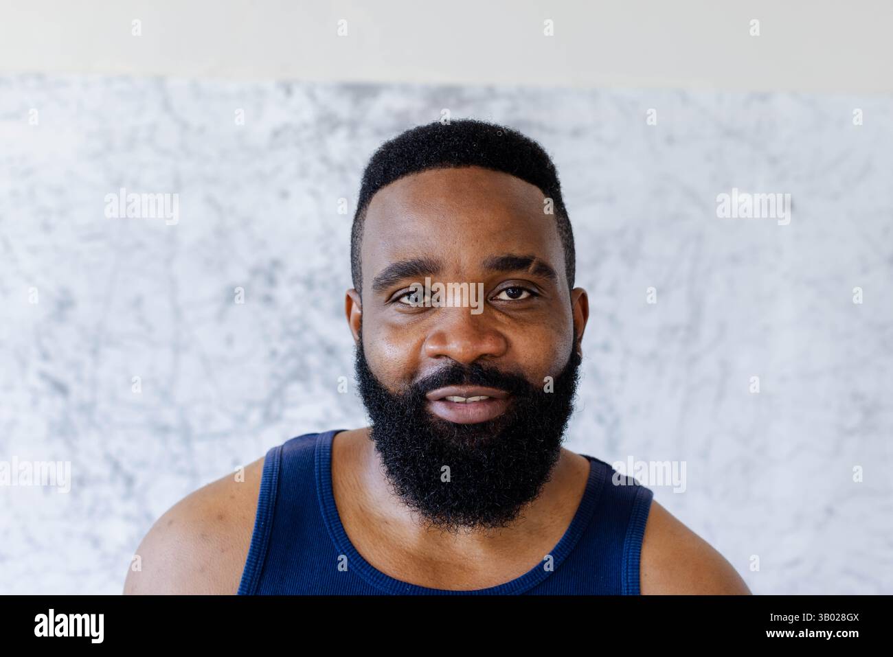 Stehender afroamerikanischer Mann mit marineblauem, athletischem Panzertop an der Marmorwand, zeigt Stärke Stockfoto
