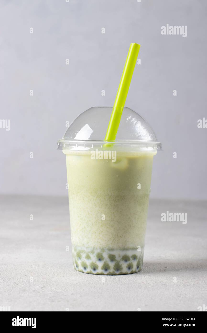 Ein Glas Eismatcha-Grüntee-Latte zum Mitnehmen mit einer Blase auf grauem Hintergrund Stockfoto