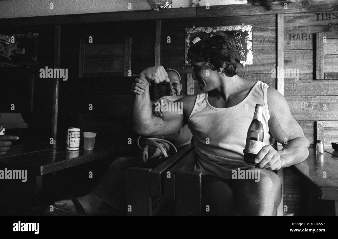 Juli 1979; Los Angeles, CA, USA; der professionelle Bodybuilder ARNOLD SCHWARZENEGGER biegt sich an die Kamera und einen Freund, während er mit ihr ein Bier trinkt. Arnold, geboren in einem kleinen Dorf in Österreich, nahm schon in jungen Jahren das Krafttraining auf und stieg bald als Bodybuilding-Champion an die Spitze. Sein Einbruch in der Schauspielerei kam 1982 in dem Film Conan the Barbarian. Seit Conan hat Arnold eine lange Karriere als Schauspieler. Arnold ist seit den frühen 80er Jahren in der US-Politik aktiv und wurde seitdem als Gouverneur von Kalifornien gewählt, weil er sich an den früheren G erinnert Stockfoto