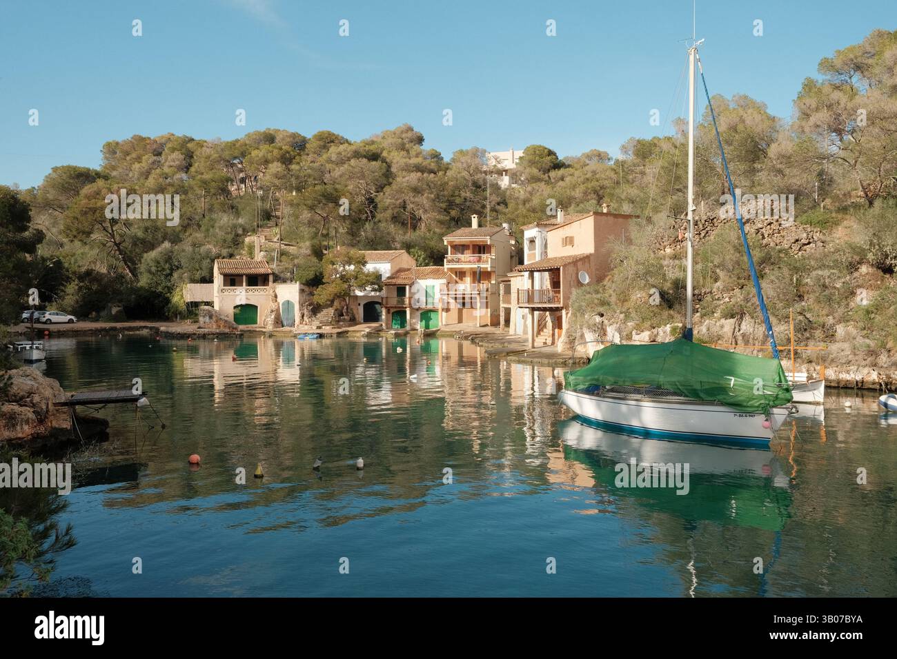 Ein grün-weißes Segelboot, das im ruhigen Hafen von Cala Figuera auf Mallorca schwimmt. Umgeben von mediterranem Wald und traditionellen Fischern Stockfoto