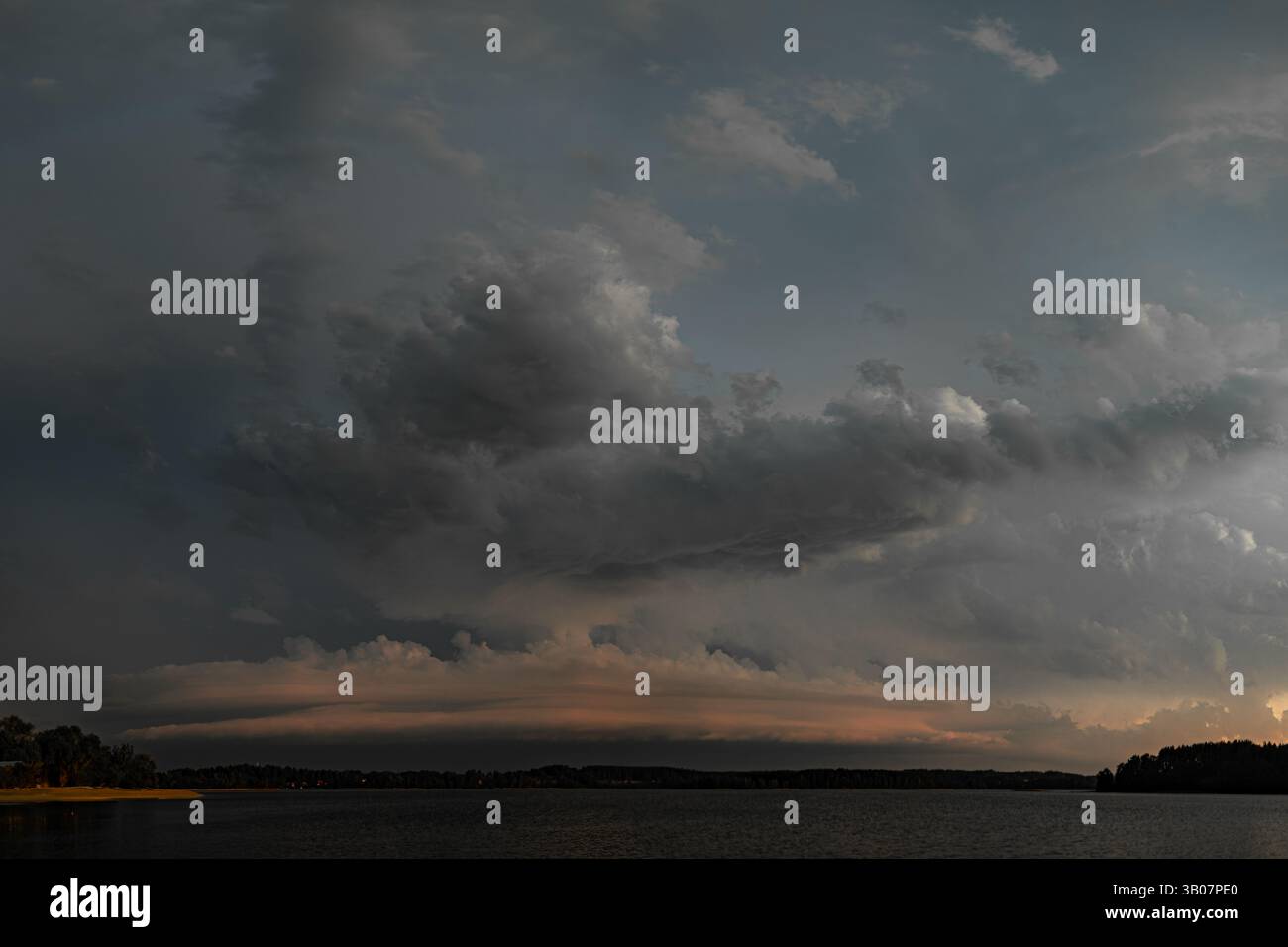 Mächtige und dramatische Szene mit dunklen Sturmwolken, die kurz vor Einbruch der Dunkelheit über einen stillen See fegen. Die schweren Wolken werden durch einen stimmungsvollen Sonnenuntergang hervorgehoben Stockfoto