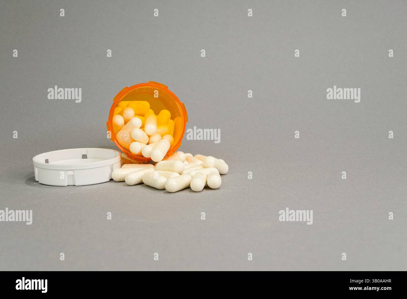 Eine offene orangefarbene verschreibungspflichtige Flasche auf der Vorderseite, auf der einige Kapseln auf grauem Hintergrund auslaufen. Stockfoto
