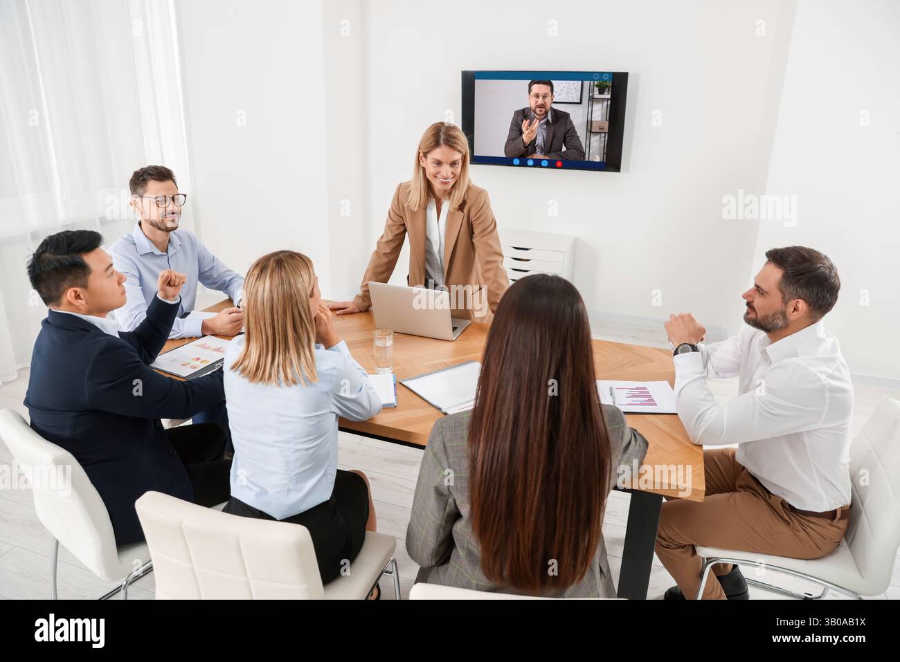 Redner, der über Online-Videochat an der Vorlesung teilnimmt. Publikum und Trainer im Konferenzraum mit Fernseher Stockfoto
