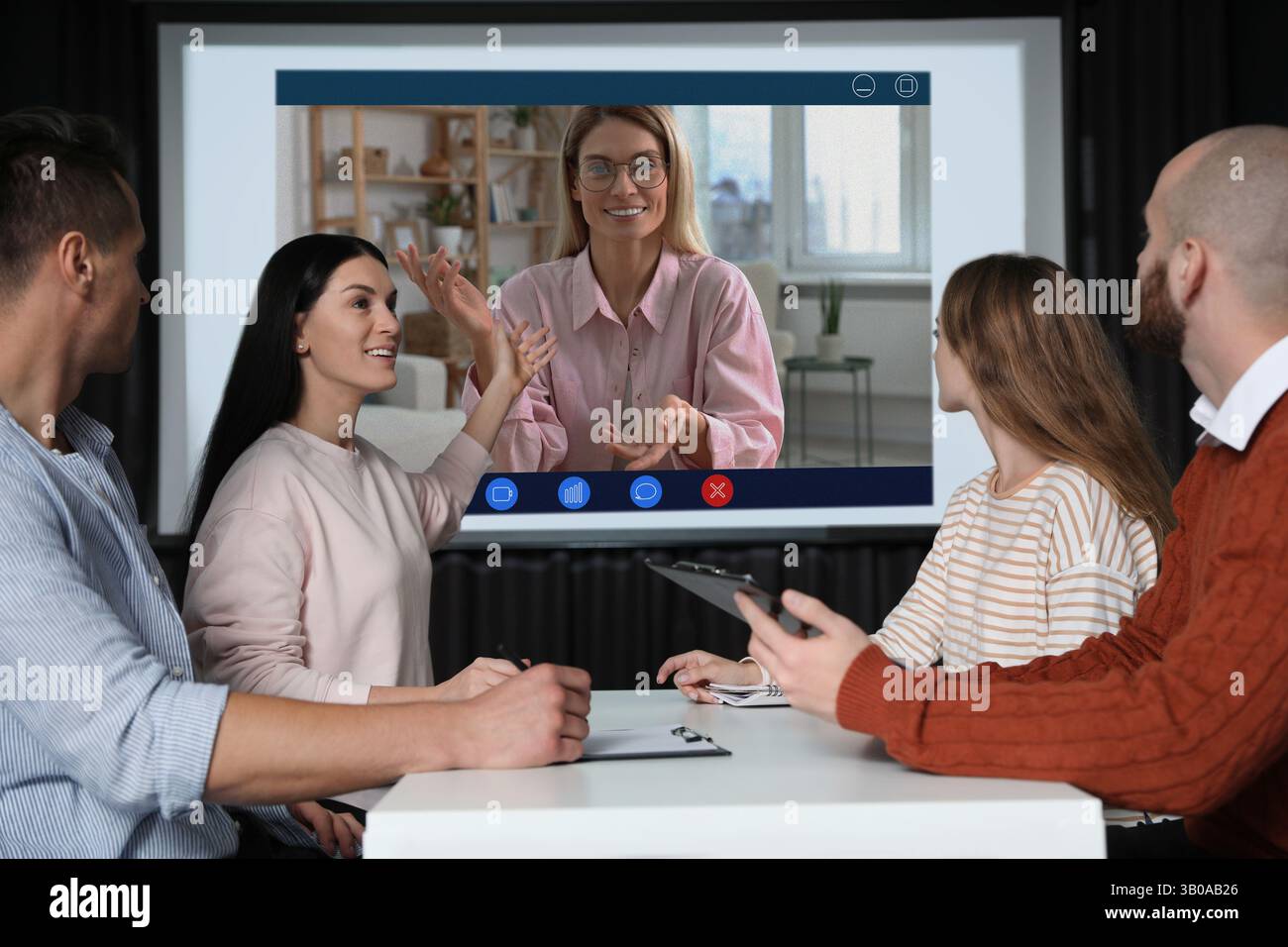Redner, der über Online-Videochat an der Vorlesung teilnimmt. Publikum im Konferenzraum mit Projektionsleinwand Stockfoto