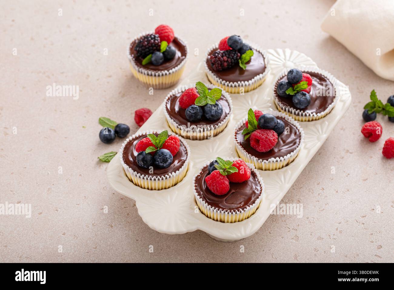 Mini-Käsekuchen in einer Muffinpfanne gebacken mit Schokoladenganache und frischen Beeren Stockfoto