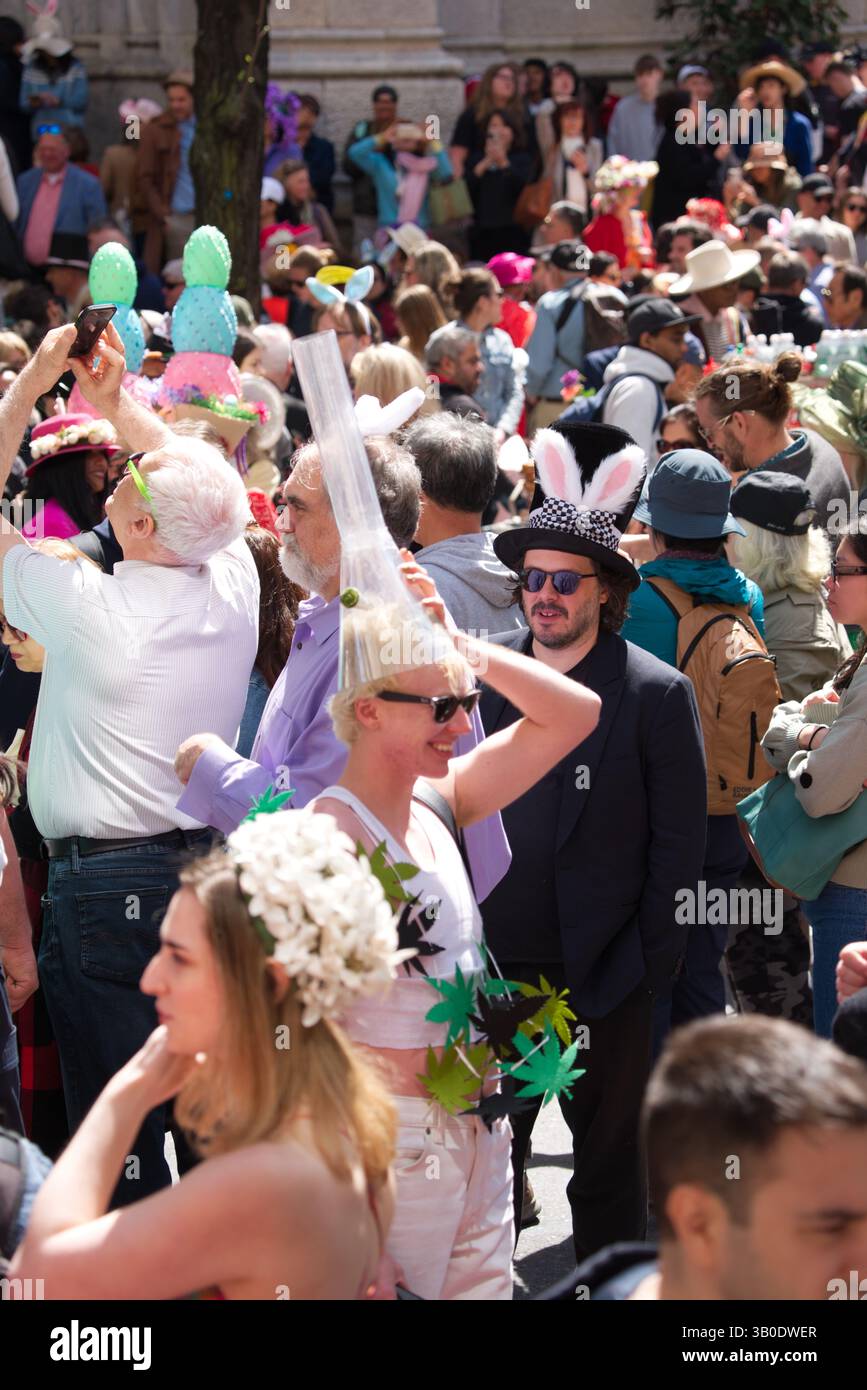 Eine lebhafte Szene im Freien bei einer festlichen Veranstaltung, bei der zahlreiche Teilnehmer Hüte und andere Kopfbedeckungen tragen. Eine Person in einem großen durchsichtigen Röhrenhut Stockfoto