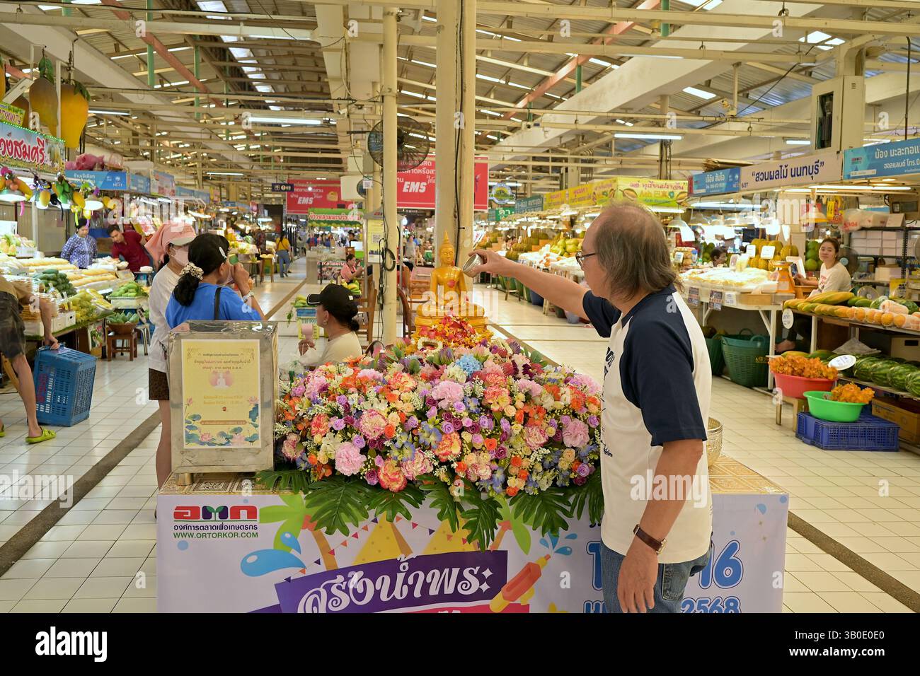 Ein Mann, der während Songkran ein rituelles Opfer von duftendem Wasser für ein Buddha-Bild auf dem beliebten Markt oder Tor Kor in Bangkok macht Stockfoto