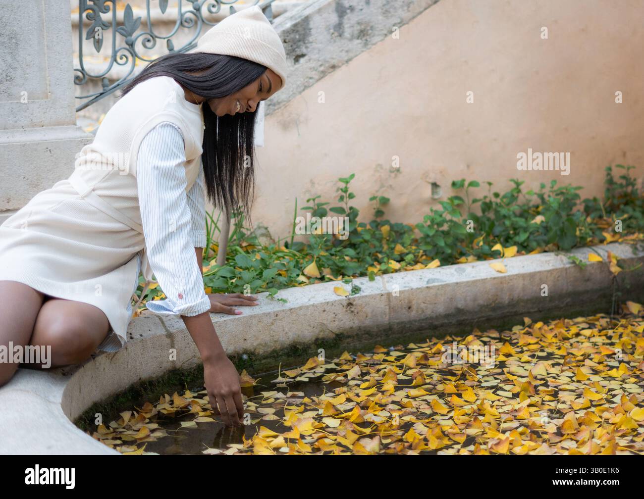Junge schwarze Frau, die Herbstblätter berührt, die im Brunnenwasser schweben Stockfoto