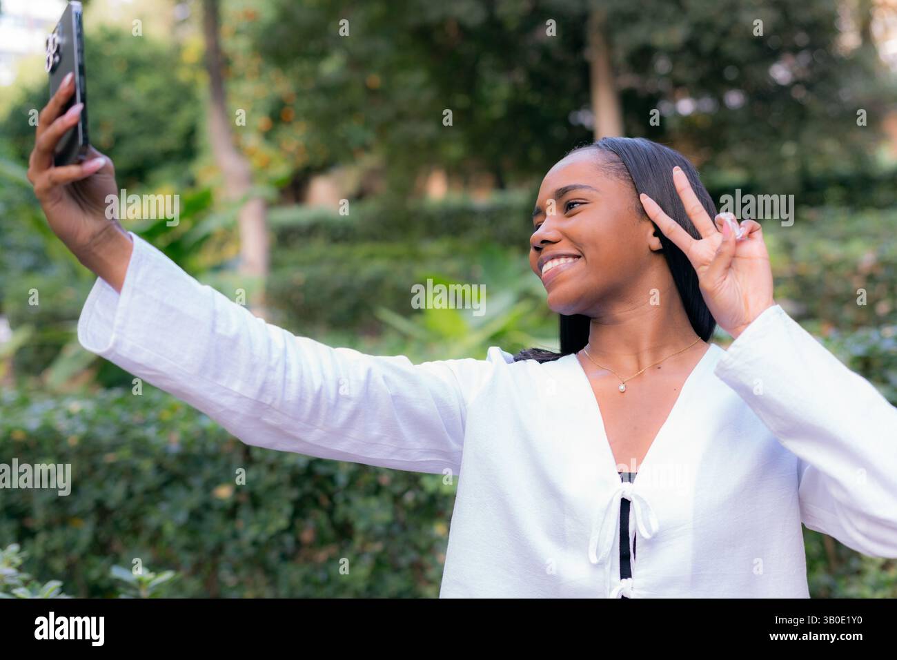 Eine junge Frau, die ein lustiges und fröhliches Selfie in einer wunderschönen und üppigen Park-Umgebung macht Stockfoto