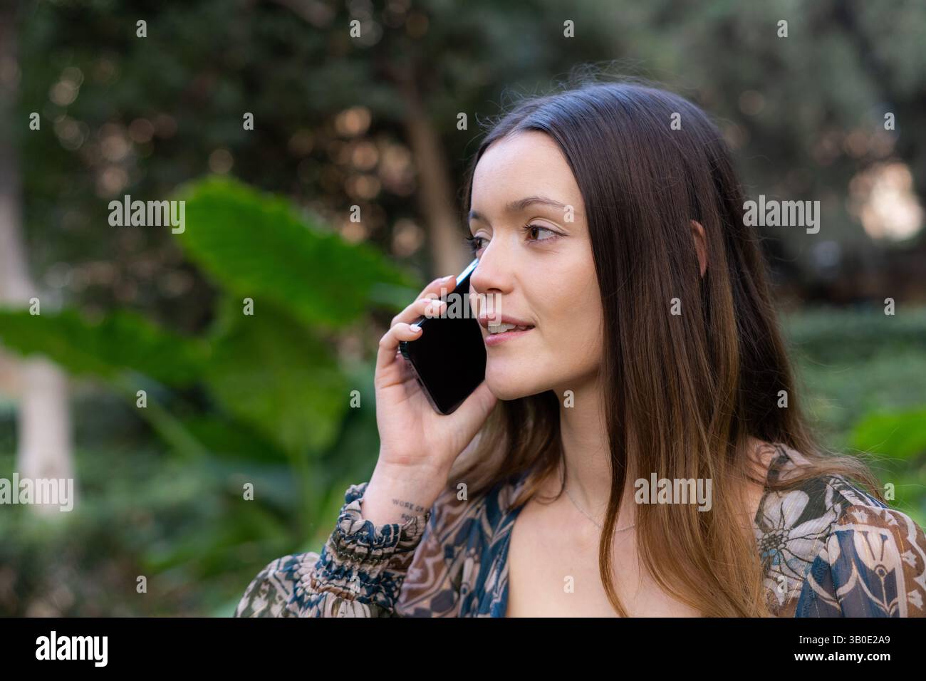 Eine Frau, die sich in ein Gespräch eingelassen hat, während sie mit ihrem Smartphone sprach, umgeben von üppigem Grün Stockfoto