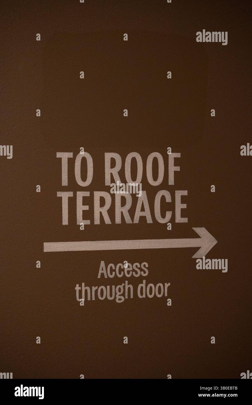 Ein Richtungsschild mit der Aufschrift „to Roof Terrace“, das an einer Wand in einem angesagten Veranstaltungsort gemalt ist. Großartiges Stockfoto für Konzepte wie Dachveranstaltungen, Essen im Freien Stockfoto