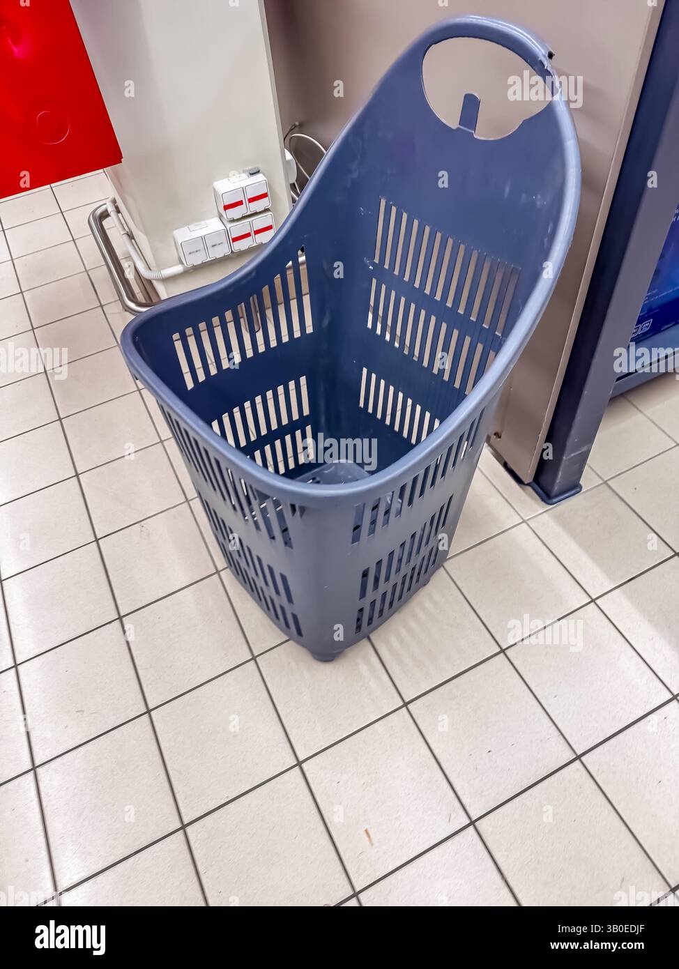 Abgenutzter blauer Kunststoffkorb mit gebrochenem Griff auf gefliestem Boden in einem Einzelhandelsgeschäft. Hochwertige Fotos Stockfoto