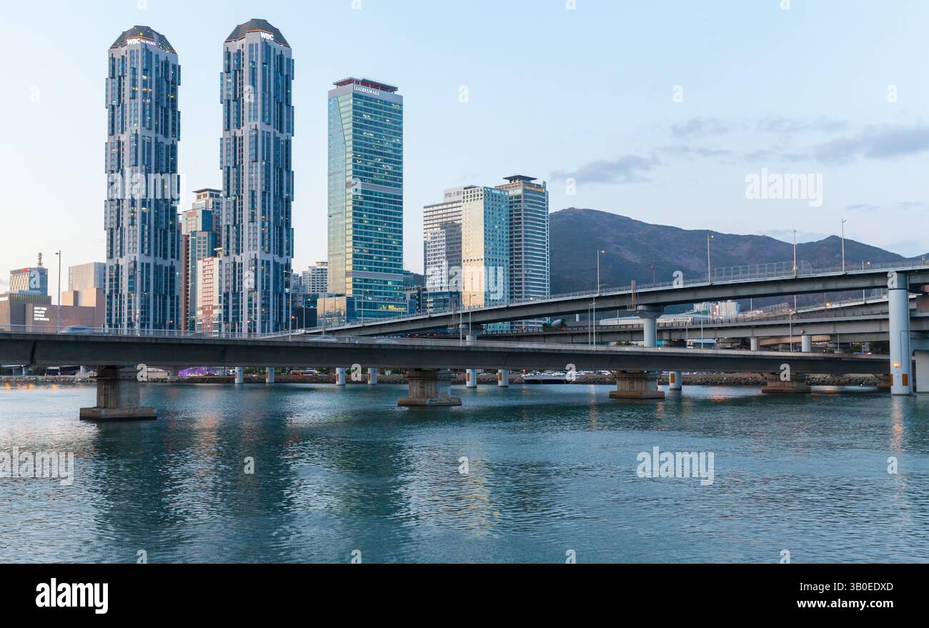 Busan, Südkorea - 16. März 2018: Modernes Stadtbild mit Wolkenkratzern, einer Brücke über ruhiges Wasser und einer bergigen Kulisse während der Dämmerung, Highl Stockfoto