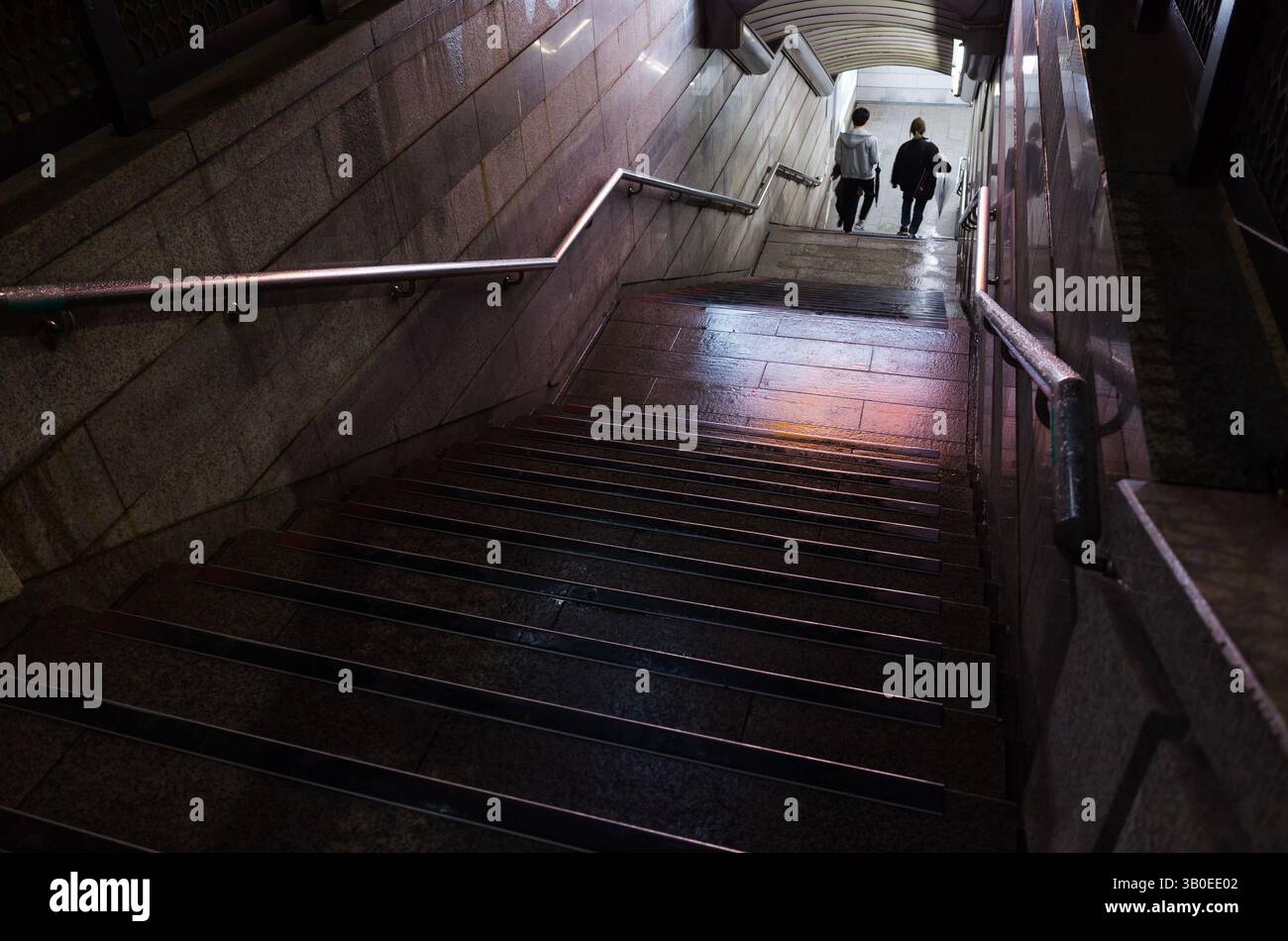 Busan, Südkorea - 19. März 2018: Schwach beleuchtete U-Bahn-Treppen führen zu einem Ausgang, während zwei Personen unter sanfter Beleuchtung hinuntergehen Stockfoto