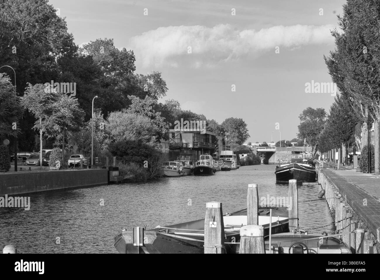 Ein ruhiger Stadtkanal mit Booten, flankiert von Bäumen und Gebäuden, schafft eine klassische, zeitlose Atmosphäre in Schwarz-weiß-Optik. Stockfoto