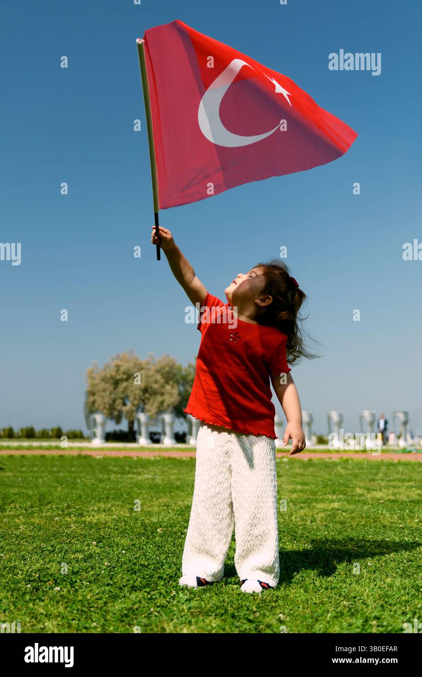 Izmir, Türkei - 23. April 2025: Ein junges Mädchen in rotem Hemd weht während der Kindertagsfeier unter dem blauen Himmel in I enthusiastisch eine türkische Flagge Stockfoto