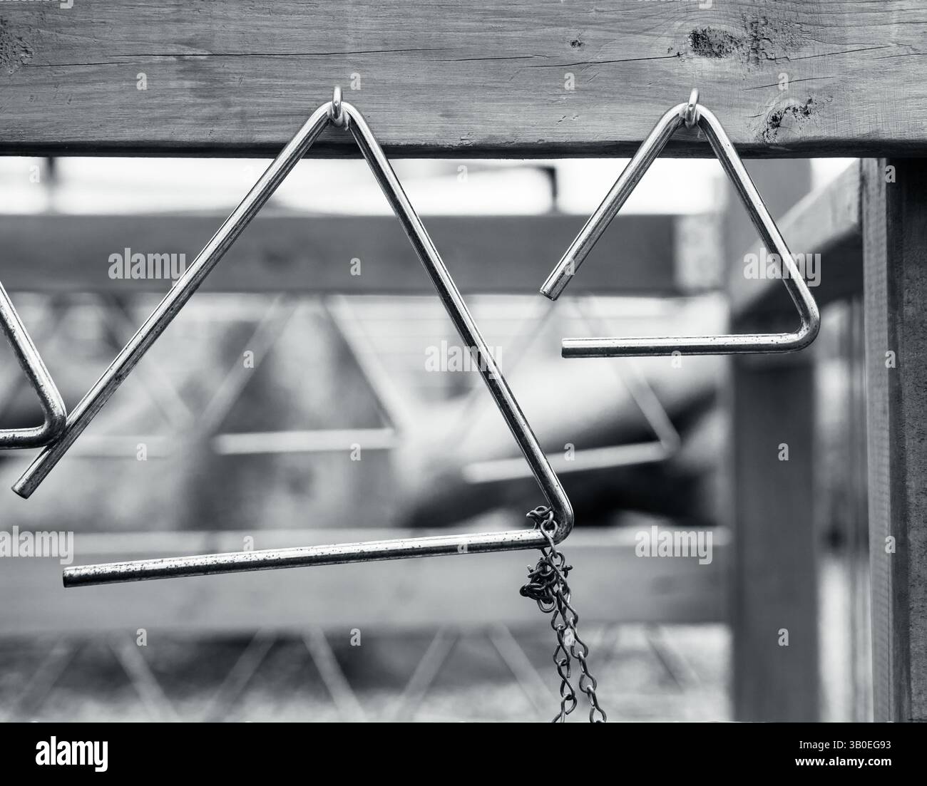 Schwarz-weiß von Metalldreiecken, die an Haken von Holzdielen im Spielplatz hängen, um Musik zu erforschen, Formen und Muster zu wiederholen Stockfoto