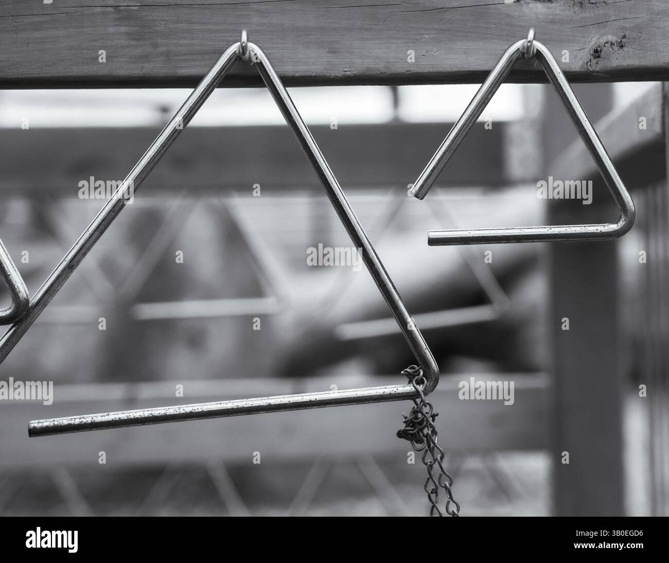 Schwarz-weiß von Metalldreiecken, die an Haken von Holzdielen im Spielplatz hängen, um Musik zu erforschen, Formen und Muster zu wiederholen Stockfoto