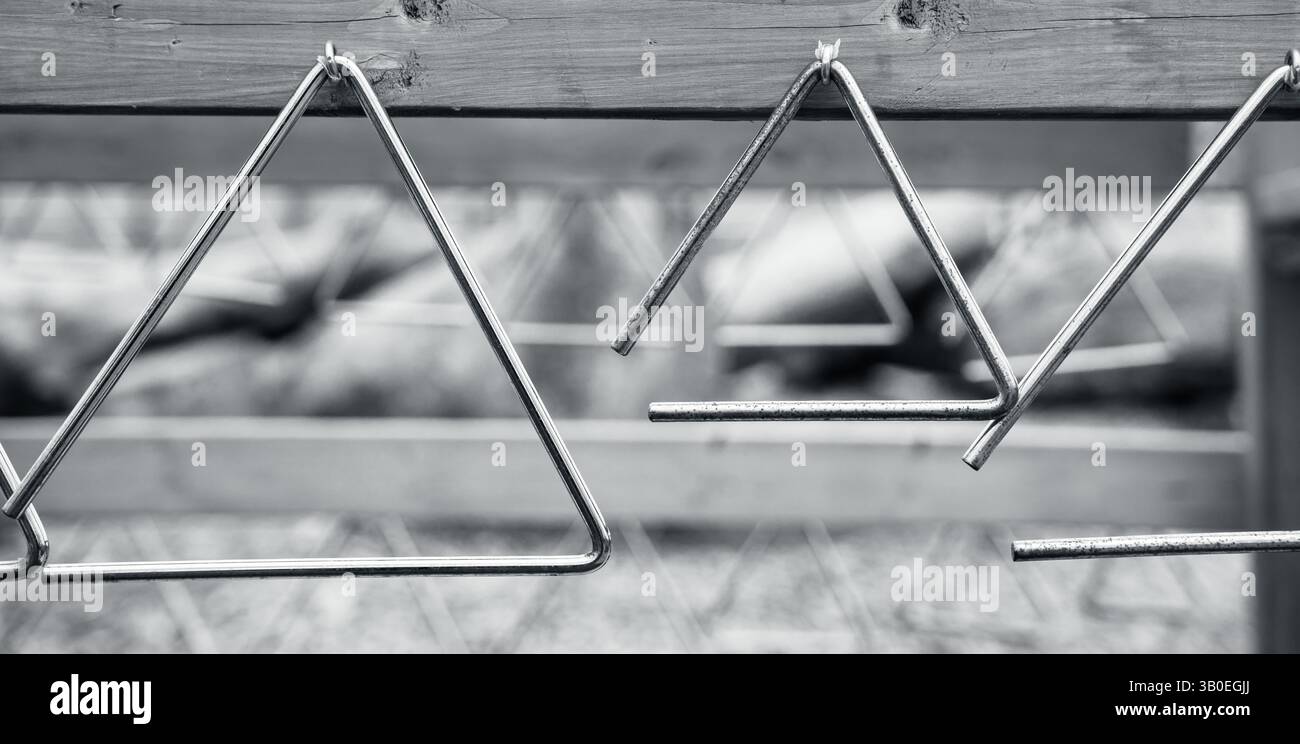 Schwarz-weiß von Metalldreiecken, die an Haken von Holzdielen im Spielplatz hängen, um Musik zu erforschen, Formen und Muster zu wiederholen Stockfoto