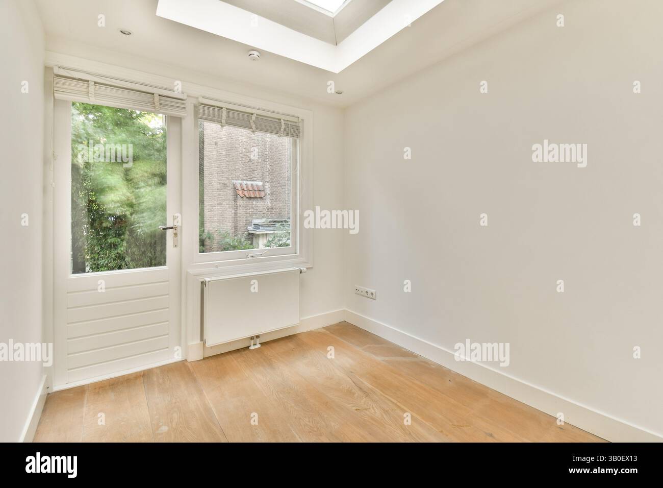 Helle, minimalistische Inneneinrichtung mit einem großen Fenster, das natürliches Licht einlädt, ergänzt durch hellen Holzfußboden und neutrale Wände. Stockfoto