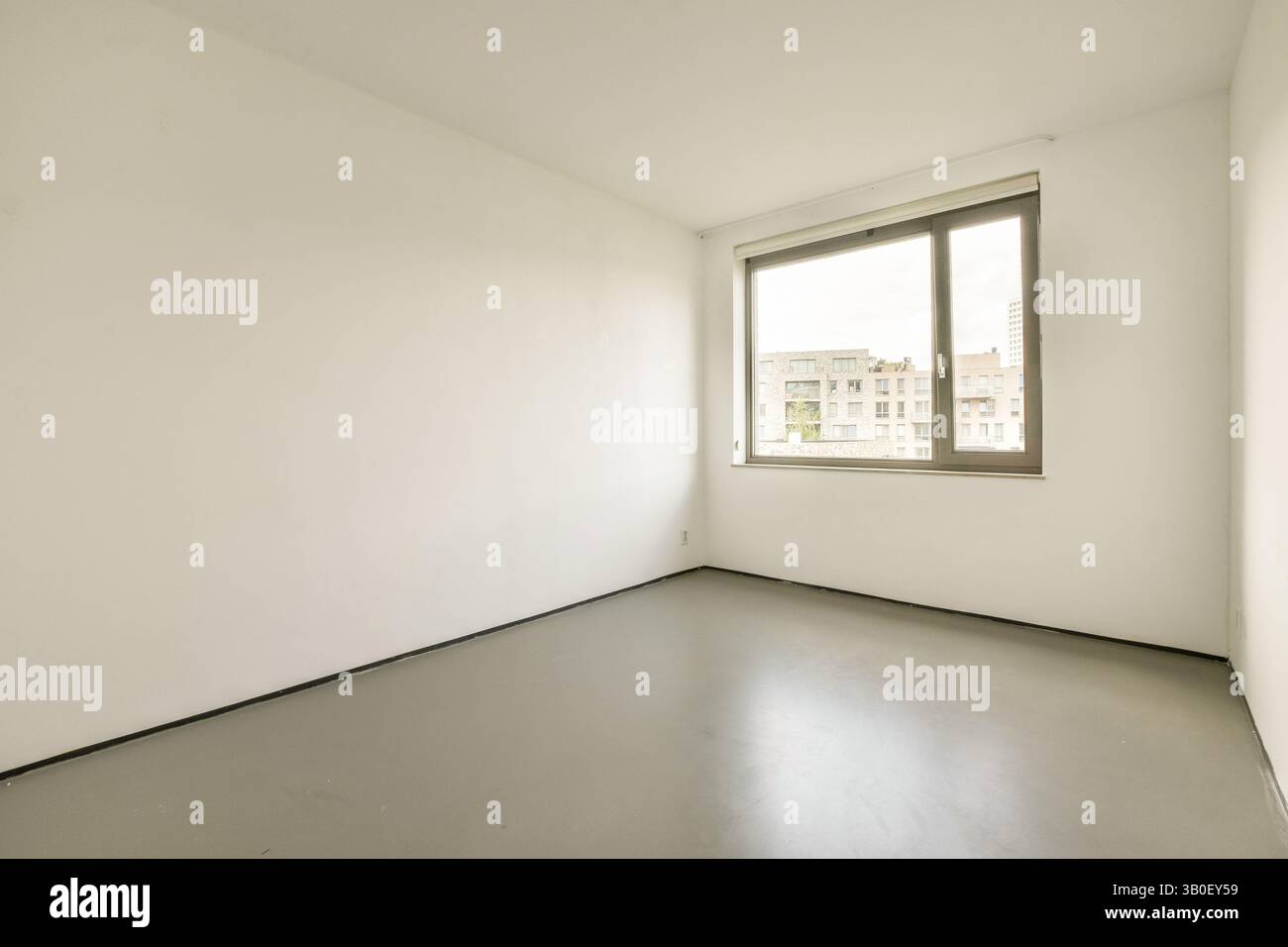 Ein heller, spärlich eingerichteter Innenraum mit großen Fenstern, durch die Tageslicht den Raum füllt. Die Wände sind schlicht und die Farben neutral. Stockfoto