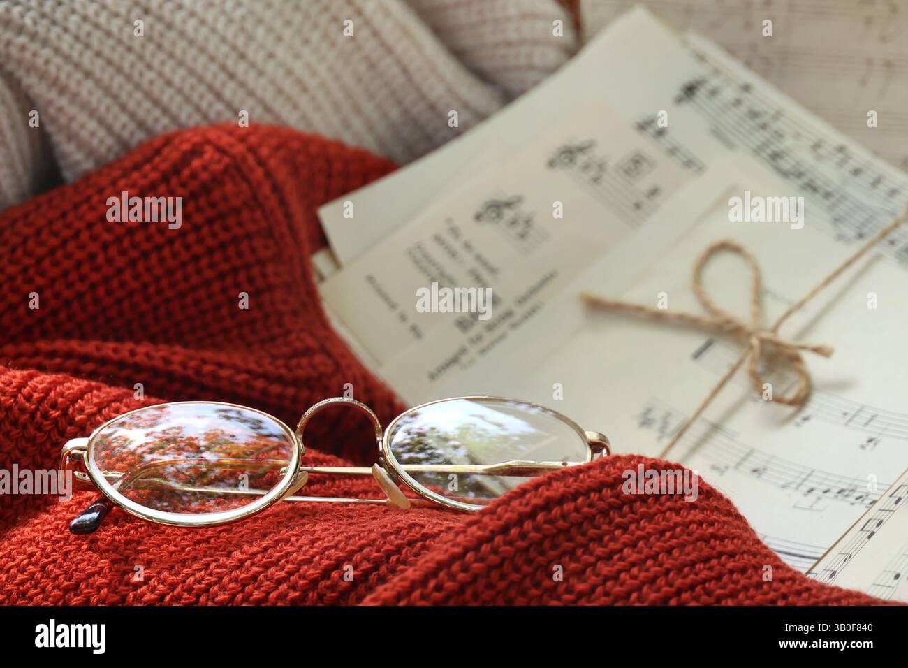 Retro-Sonnenbrille im herbstlichen Setting auf einem orangefarbenen Garnpullover mit Notenblättern im Hintergrund. Stockfoto