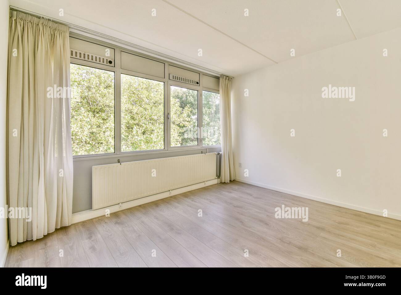 Ein geräumiger, unmöblierter Raum mit großen Fenstern, die natürliches Licht hereinlassen und die neutralen Farben der Wände und des Holzfußbodens hervorheben. Stockfoto